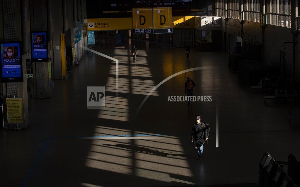 A few people walk through an empty corridor inside the Sao Paulo International Airport in Guarulhos, Brazil, Wednesday, May 27, 2020. According to the airport administration, Brazil's busiest airport has had an average reduction of 85% in flights, due to the COVID-19 pandemic. (AP Photo/Andre Penner)