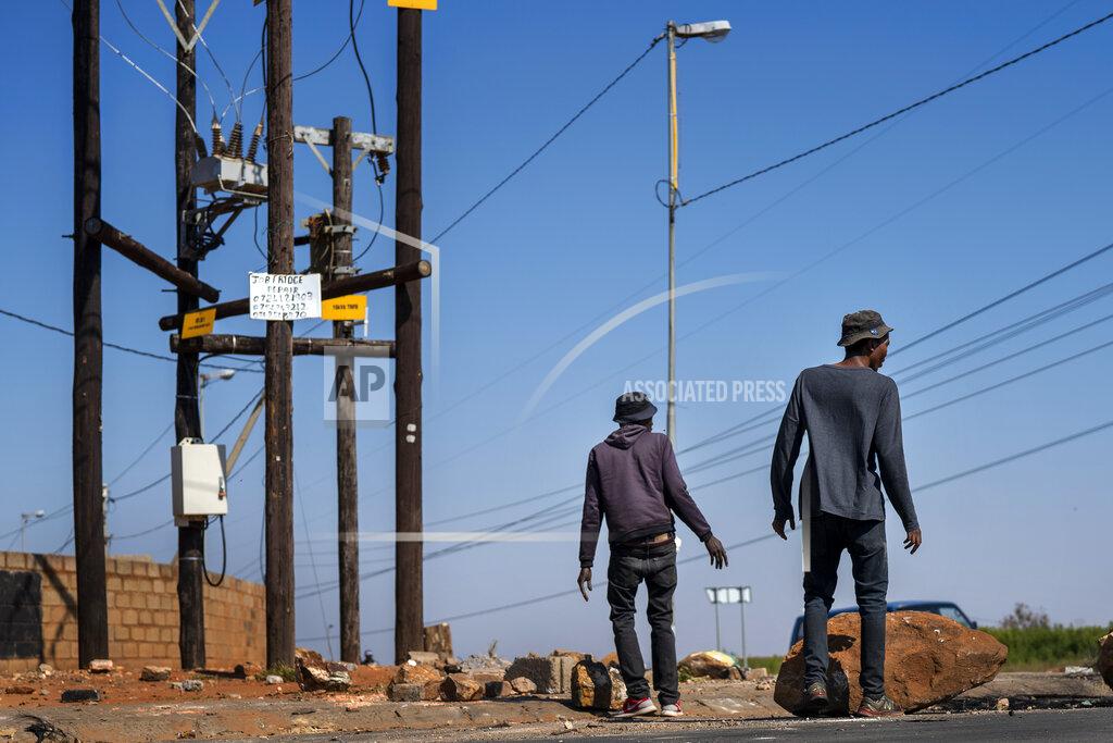 Jerome Delay FILE- In this file photo taken Wednesday May 13, 2020, residents of the Snake Park neighborhood of Soweto outside Johannesburg, South Africa, walk through debris following a protest. South Africa is struggling to balance its fight against the coronavirus with its dire need to resume economic activity. The country with the Africa’s most developed economy also has its highest number of infections — more than 19,000. (AP Photo/Jerome Delay, File)