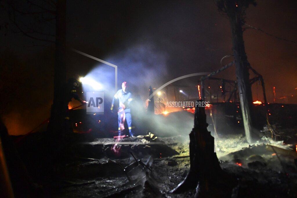 Michael Svarnias Firefighters try to extinguish the flames at makeshift tents outside the perimeter of the overcrowded refugee camp at the port of Vathy on the eastern Aegean island of Samos, Greece, late Sunday, Sept. 19, 2021. A fire has broken out at a soon-to-be-closed migrant camp on the Greek island of Samos, forcing its evacuation. The transfer of the migrants to the new, €43 million ($50 million) facility was due to begin Monday and be completed by Wednesday. (AP Photo/Michael Svarnias)