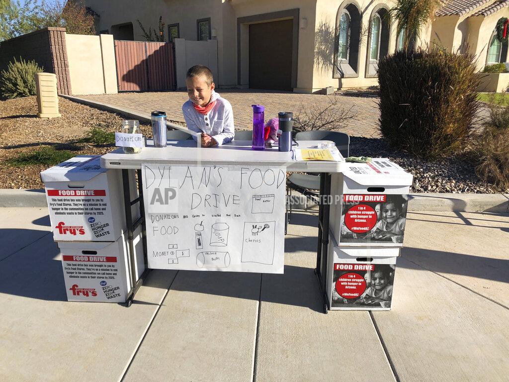 Dylan Pfeifer sits on the corner of his neighborhood cul da sac in Chandler, Ariz., Saturday, Dec. 5, 2020. Pfeifer received 555 cans and boxes and about $500 in monetary donations. (Erin Pfeifer via AP)