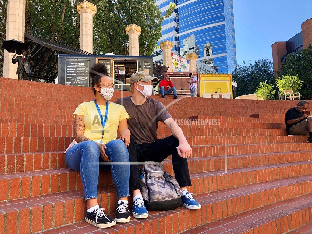 Gillian Flaccus Isabelle Eley and her boyfriend Benjamin Green sit in Pioneer Courthouse Square, Aug. 27, 2020 in Portland, Ore. Green, a forklift operator in the Portland suburb of Beaverton, said he felt safe in the city and enjoyed his visit despite boarded up windows and graffiti from recent protests. "It's a pretty day and we feel just perfectly safe as long as we've got our masks on," said Green. "I don't see why there's any need to be scared to walk around out here." (AP Photo/Gillian Flaccus)