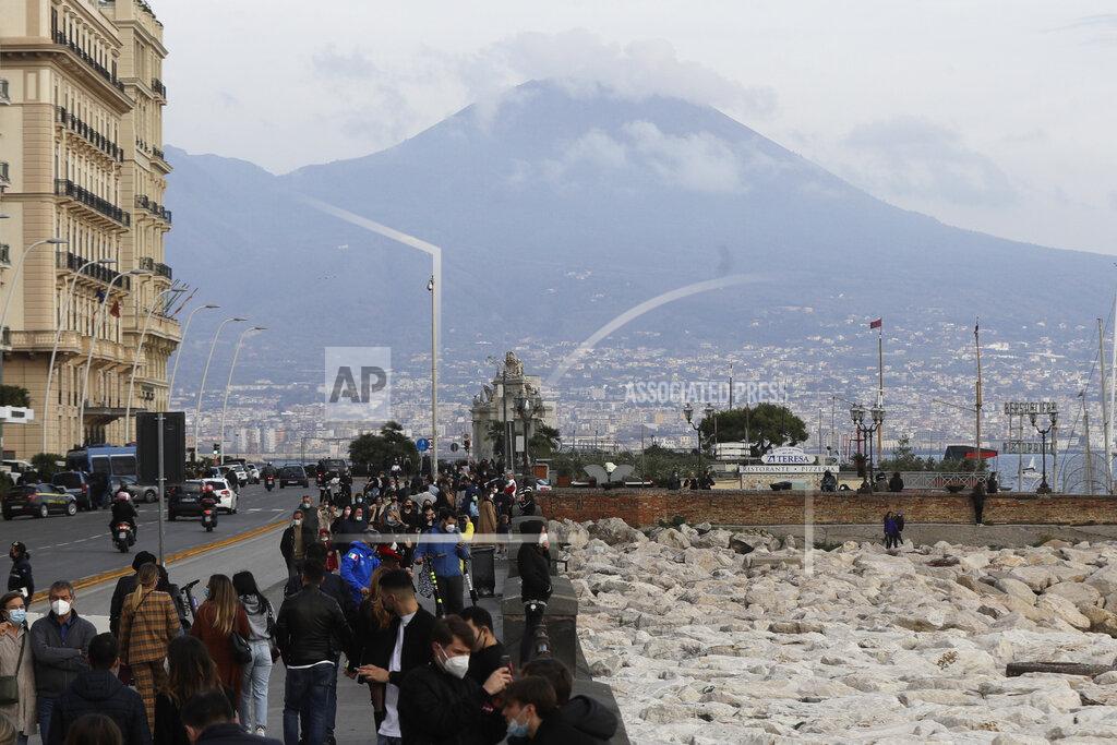 Gregorio Borgia People stroll along Viale Caracciolo overlooking the Gulf of iNaples, Italy, Saturday, Nov. 14, 2020. Along the Naples waterfront, Luigi Orefice perched his 4-year-old son, Giovanni, on the thick wall lining the promenade. With fog ringing the Vesuvius volcano in the background, the postcard-like panorama would be familiar to tourists. But his job delivering beverages to hospitals lets Orefice see the ugly realities beyond the “O Sole Mio” image tourists might have of the south. (AP Photo/Gregorio Borgia)