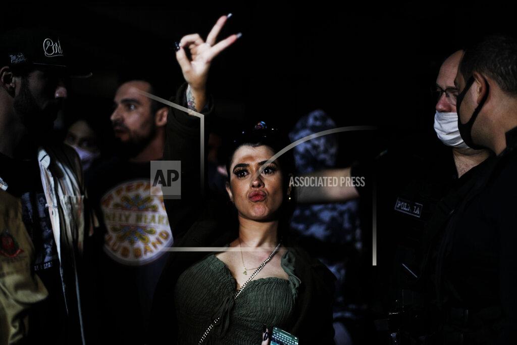 Marcelo Chello A woman flashes a V sign as police break up a social gathering during an operation against illegal and clandestine gatherings that authorities believe are partly responsible for fueling the spread of COVID-19, at a party hall in Sao Paulo, Brazil, early Saturday, April 17, 2021. (AP Photo/Marcelo Chello)