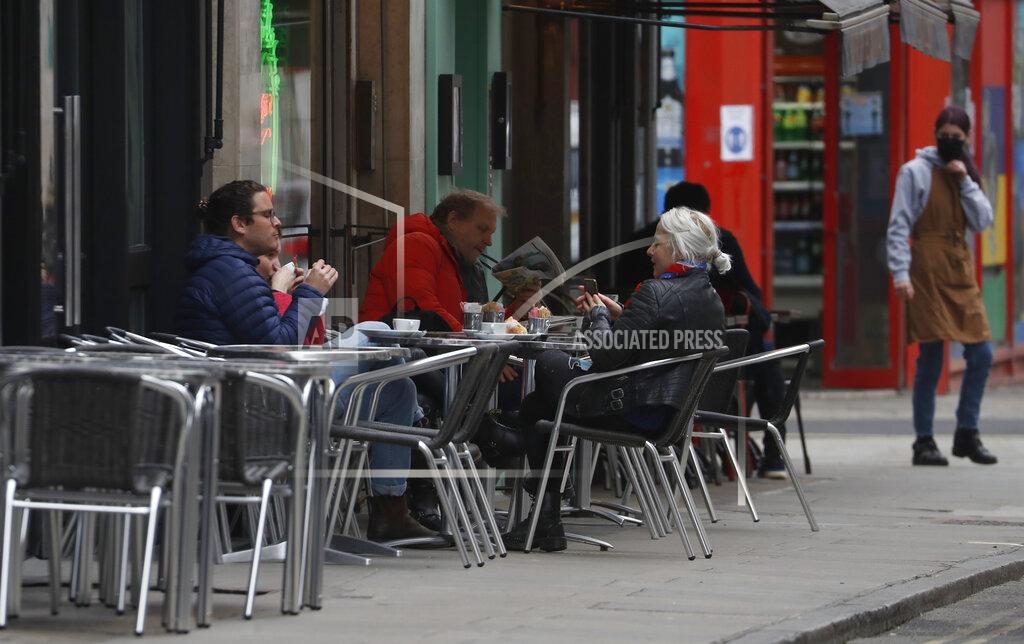 Alastair Grant A waitress looks at her customers as they sit outside a cafe while preparations get underway in the Soho area of London, Monday, April 12, 2021, as restaurants, bars and pubs can open and serve people who can be seated outside. Millions of people in England will get their first chance in months for haircuts, casual shopping and restaurant meals on Monday, as the government takes the next step on its coronavirus lockdown-lifting road map. (AP Photo/Alastair Grant)
