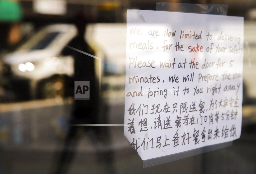 Jim Slosiarek In this Wednesday, April 1, 2020, photo, a sign, in English and Chinese, on the front door of Yummy Restaurant on the Ped Mall tells customers to wait while their food is being prepared and will be brought out in Iowa City, Iowa. Restaurants and businesses are trying to generate revenue amid the coronavirus shutdown by offering delivery or curbside carry-out. (Jim Slosiarek/The Gazette via AP)