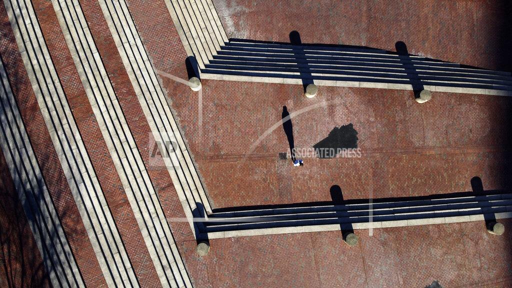 David Goldman The late afternoon sun casts a long shadow of a lone pedestrian walking up the steps of City Hall Plaza, Saturday, March 21, 2020, in Boston. From above, life on earth looks different. The patterns of our daily routines are now replaced by the patterns of the long shadows of solitary figures in the early spring sunshine. (AP Photo/David Goldman)