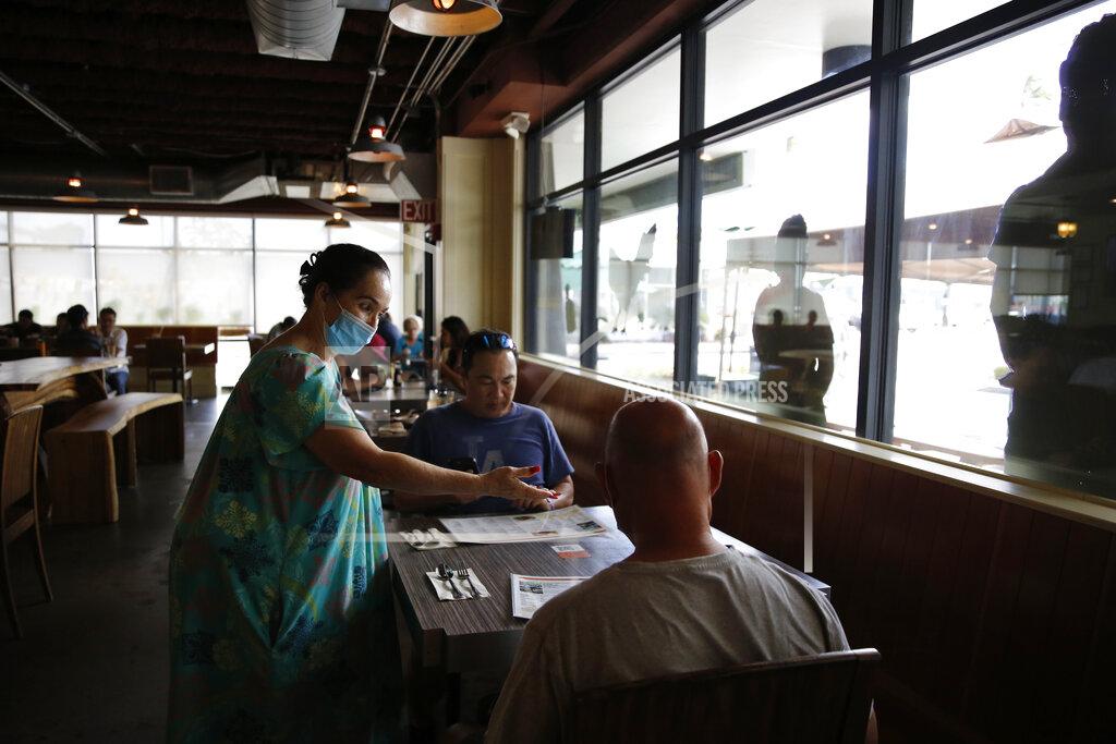 Caleb Jones Highway Inn restaurant hostess Ku'uipo Lorenzo, left, seats two customers after they showed proof of vaccination on Monday, Oct. 25, 2021, in Honolulu. To comply with local mandates, the restaurant requires all indoor diners to show proof of vaccination or have a recent negative test result before being seated. (AP Photo/Caleb Jones)