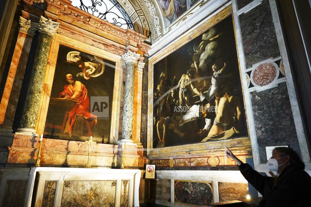 Andrew Medichini A woman wearing a face mask to curb the spread of COVID-19 points to a cycle of paintings by 16th century artist Michelangelo Merisi, known as Caravaggio, on the life of St.Matthew, inside the Contarelli chapel of San Luigi dei Francesi Church, in Rome, Friday, Dec. 11, 2020. Like elsewhere in Europe, museums and art galleries in Italy were closed this fall to contain the spread of COVID-19, meaning art lovers must rely on virtual tours to catch a glimpse of the treasures held by famous institutions such as the Uffizi in Florence and the Vatican Museums in Rome. However, some exquisite gems of Italy's cultural heritage remain on display in real life inside the country's churches, some of which have collections of renaissance art and iconography that would be the envy of any museum. (AP Photo/Andrew Medichini)