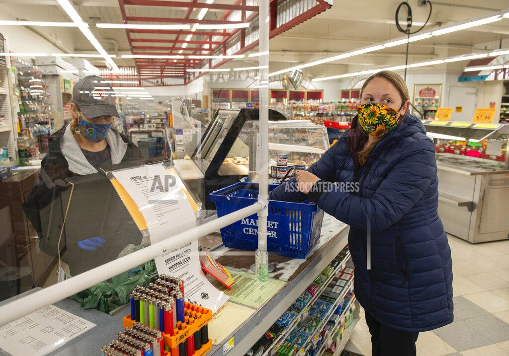 James Poulson Amanda Johnson buys food at Market Center in Sitka, Alaska, Friday, April 24, 2020, as Stephanie Larsen works behind a sheet of plexiglass. Many workers and shoppers are wearing face masks during the coronavirus pandemic as they go through their daily routines. (James Poulson/The Daily Sitka Sentinel via AP)