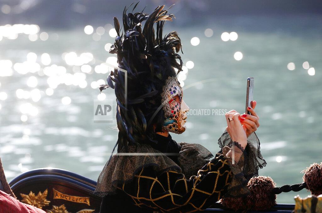 Antonio Calanni A masked woman checks her smartphone as she sits in a gondola during the water parade of the Venice Carnival in Venice, Italy, Sunday, Feb. 17, 2019. The event in the historic lagoon city attracts people from around the world. (AP Photo/Antonio Calanni)