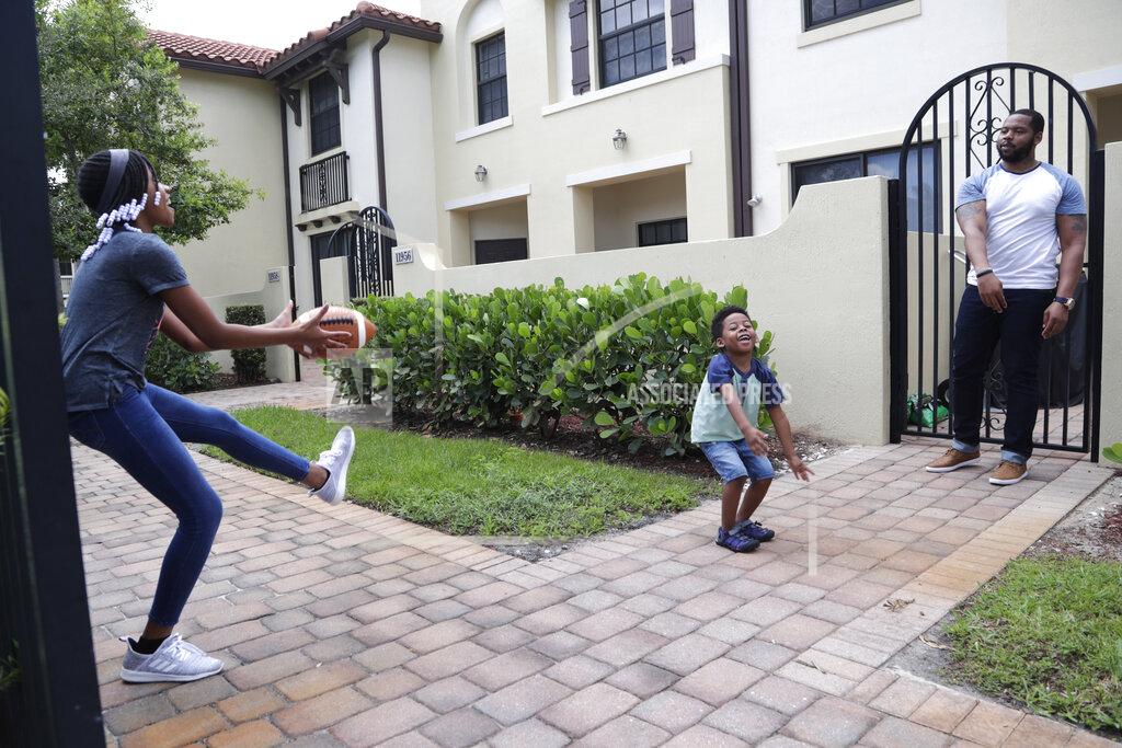 Lynne Sladky In this Tuesday, June 16, 2020 photo, D.J. Boldin, right, throws a football with his children Madison, 10, left, and Dallas, 4, center, outside of their home in Miramar, Fla. Boldin is the football coach at Pahokee High School, a predominantly black school located alongside Lake Okeechobee in Florida. Recent events have given Boldin an opportunity to use his position to prepare his players for the challenges they will face when they leave the bubble that is their small town. (AP Photo/Lynne Sladky)