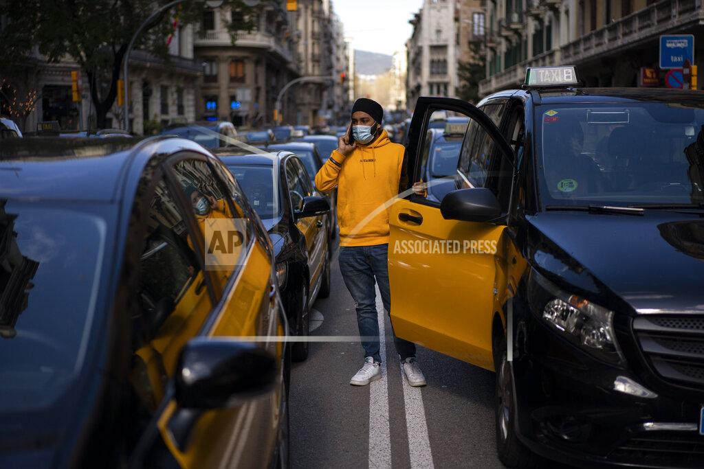 Emilio Morenatti A taxi driver stands next to his cab as they march slowly blocking the traffic along one of the avenues in Barcelona downtown, Spain, Thursday, March 18, 2021. Hundreds of yellow-and-black cabs disrupted Barcelona's road traffic on Thursday to protest against the return of the ride-hailing giant Uber to the northeastern city after a 2-year hiatus. (AP Photo/Emilio Morenatti)