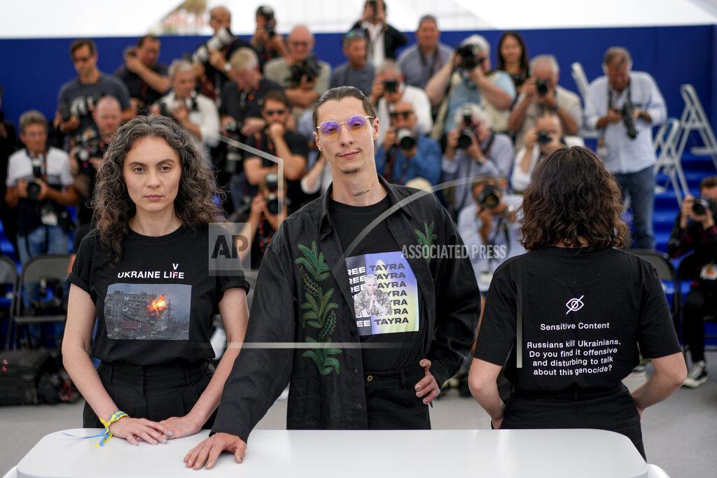 Daniel Cole Producers Darya Bassel, left, and Yelizaveta Smith, right, wearing t-shirts that have an image of an explosion on the front and read "Sensitive Content: Russians kill Ukrainians. Do you find it offensive and disturbing to talk about this genocide?" pose with director Maksym Nakonechnyi who wears a t-shirt that reads "Free Tayra" in reference to Julia Paevska, aka Tayra, a Ukrainian medic who Russian forces have taken captive at the photo call for the film 'Butterfly Vision' at the 75th international film festival, Cannes, southern France, Wednesday, May 25, 2022. (AP Photo/Daniel Cole)
