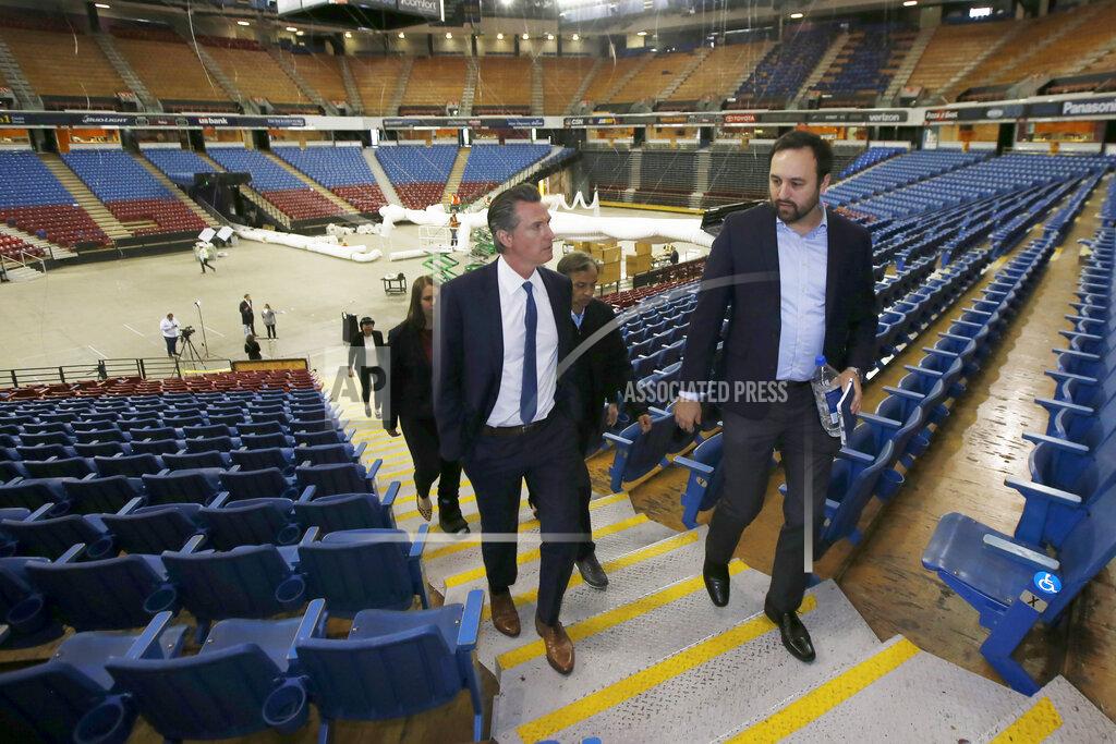 FILE - In this April 6, 2020, file photo, California Gov. Gavin Newsom, left, accompanied by Jason Kenney, deputy director of the Real Estate Services Division of the Department of General Services, tours Sleep Train Arena while it was being transformed into a 400-bed emergency field hospital in Sacramento, Calif. About a year after the state's first coronavirus case, Newsom has gone from a governor widely hailed for his swift response to a leader facing criticism from all angles. (AP Photo/Rich Pedroncelli, Pool, File)