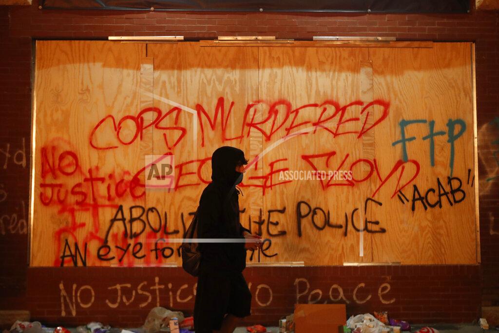 John Minchillo A person walks past a building covered with graffiti Thursday, May 28, 2020, in Minneapolis. Protests over the death of George Floyd, a black man who died in police custody Monday, broke out in Minneapolis for a third straight night. (AP Photo/John Minchillo)