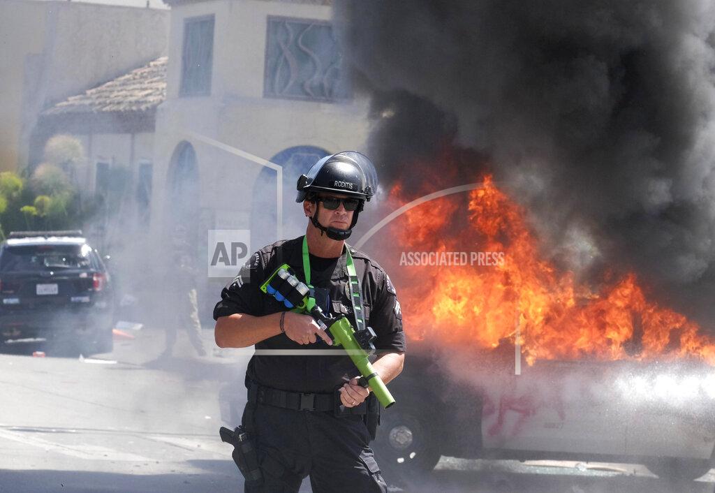 Ringo H.w. Chiu A police officer stands guard while a police vehicle burns during a protest over the death of George Floyd in Los Angeles, Saturday, May 30, 2020. Protests across the country have escalated over the death of George Floyd who died after being restrained by Minneapolis police officers on Memorial Day, May 25.(AP Photo/Ringo H.W. Chiu)