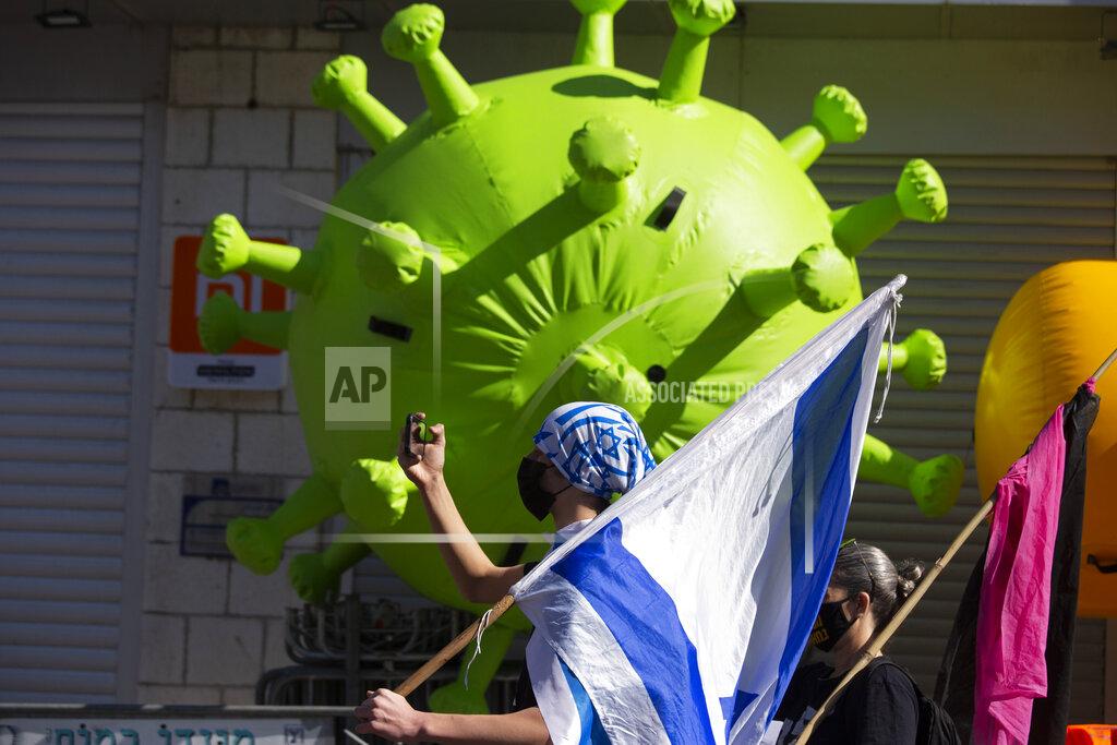 Maya Alleruzzo A protester wearing the colors of the Israeli flag poses for a selfie in front of a giant representation of the coronavirus outside the District Court, during a hearing in Israeli Prime Minister Benjamin Netanyahu's corruption trial, in Jerusalem, Monday, Feb. 8, 2021. Netanyahu has pleaded not guilty as his trial on corruption charges resumes in a Jerusalem courtroom just weeks before national elections in which he hopes to extend his 12-year rule. (AP Photo/Maya Alleruzzo)