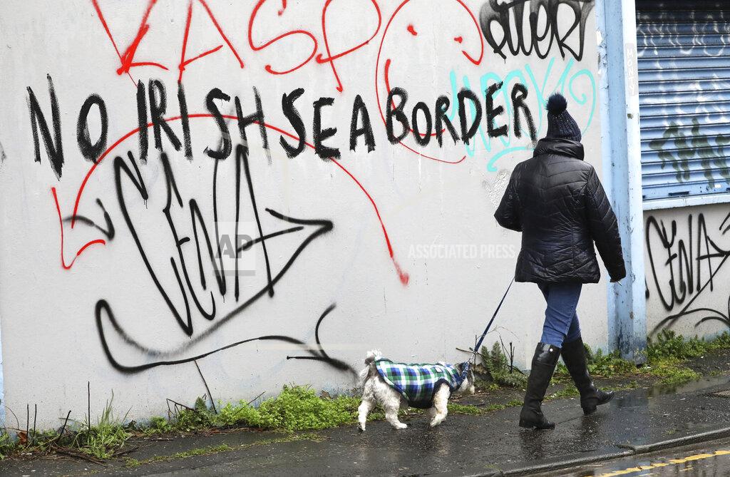 Peter Morrison A woman walks her dog past past graffiti with the words 'No Irish Sea Border' in Belfast city centre, Northern Ireland, Wednesday, Feb. 3, 2021. Politicians from Britain, Northern Ireland and the European Union are meeting to defuse post-Brexit trade tensions that have shaken Northern Ireland’s delicate political balance. British Cabinet minister Michael Gove, European Commission Vice President Maros Sefcovic and the leaders of Northern Ireland’s Catholic-Protestant power-sharing government will hold a video conference to discuss problems that have erupted barely a month after the U.K. made an economic split from the 27-nation EU. (AP Photo/Peter Morrison)