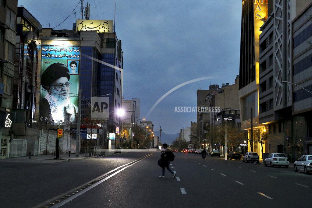 Ebrahim Noroozi A pedestrian crosses an empty street in Tehran, Iran, on Tuesday, March 24, 2020, with a portrait of Iran's Supreme Leader Ayatollah Ali Khamenei at right. Due to the coronavirus and the COVID-19 illness it causes, life has changed dramatically on Tehran's main highways, in the narrow corridors of its historical Grand Bazaar and in the public spaces under portraits of its leaders. (AP Photo/Ebrahim Noroozi)