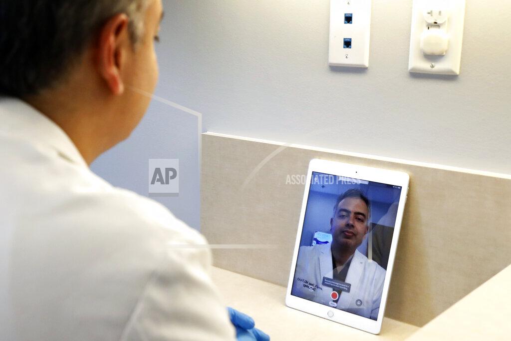 Tony Gutierrez Dermatologist Dr. Seemal Desai poses for a photo in an examination room in his office in Plano, Texas, Thursday, May 7, 2020. Desai uses the privacy of an examination room and a tablet computer to virtually visit with some of his patients. (AP Photo/Tony Gutierrez)