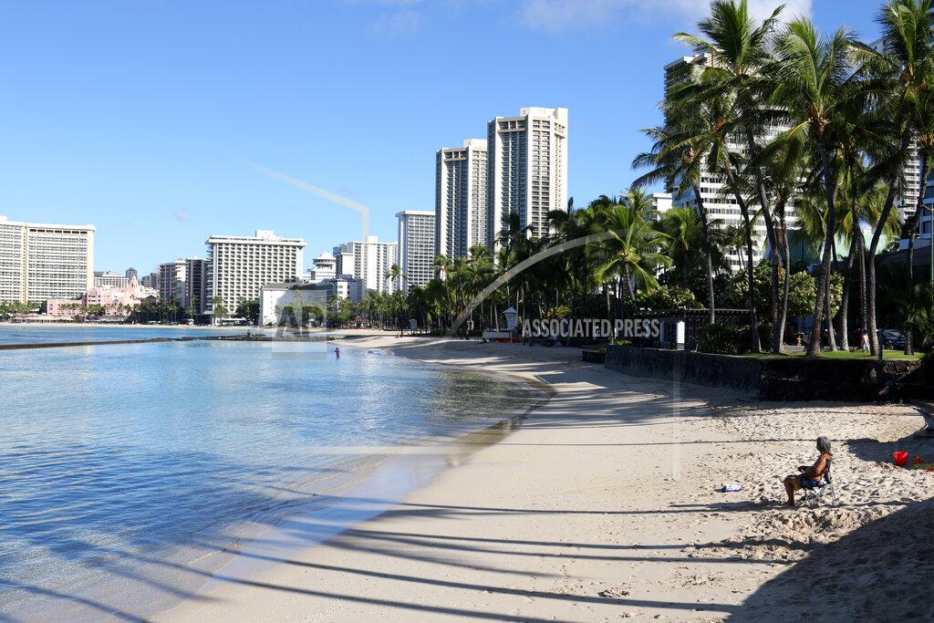 Caleb Jones FILE — In this Oct. 2, 2020, file photo, a man sits on a nearly empty Waikiki Beach in Honolulu before the state reopened its economy. After loosening rules, health care workers in Hawaii now say a lack of government action is worsening an already crippling surge of coronavirus cases in the islands, and without effective policy changes the state's limited hospitals could face a grim crisis. (AP Photo/Caleb Jones, File)