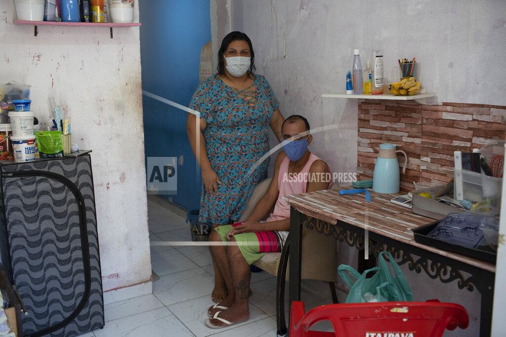 Silvia Izquierdo Rachel de Lima Ribeiro, who recovered from COVID-19, poses for a photo with her handicapped husband Felipe da Silva inside their small home in the Mare Complex favela in Rio de Janeiro, Brazil, Thursday, April 8, 2021. Ribeiro, who used to sell sweetmeats, lost her livelihood during the pandemic and now the couple eats thanks to donations. (AP Photo/Silvia Izquierdo)