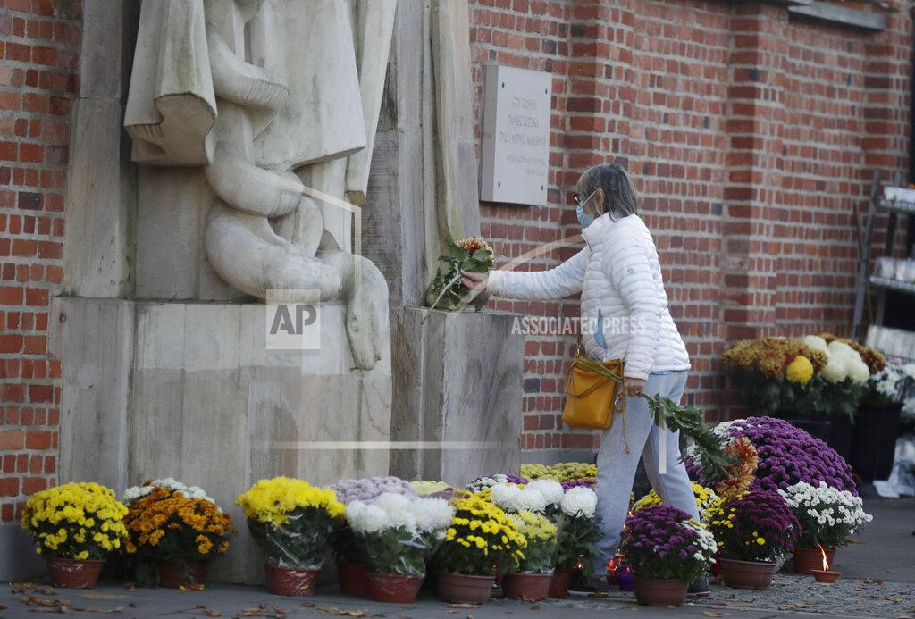 Flowers and candles people have placed outside of Powazki cemetery after Poland's government closed all cemeteries in an attempt to curb the spread of COVID-19, in Warsaw, Poland, Sunday, Nov. 1, 2020. Driven by new solidarity, Poles have been buying armloads of chrysanthemums to help out flower vendors who unexpectedly faced bankruptcy when the government ordered all cemeteries locked due to COVID-19 during a traditional memorial weekend. (AP Photo/Czarek Sokolowski)