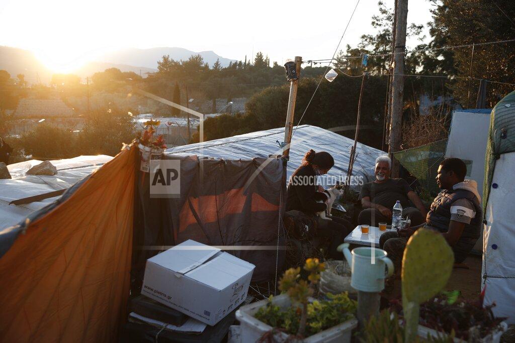 Thanassis Stavrakis Migrants sit outside of a makeshift tent as the suns sets outside the perimeter of the overcrowded refugee camp at the port of Vathy on the eastern Aegean island of Samos, Greece, Tuesday, Feb. 23, 2021. On a hill above a small island village, the sparkling blue of the Aegean just visible through the pine trees, lies a boy’s grave. His first ever boat ride was to be his last - the sea claimed him before his sixth birthday. His 25-year-old father, like so many before him, had hoped for a better life in Europe, far from the violence of his native Afghanistan. But his dreams were dashed on the rocks of Samos, a picturesque Greek island almost touching the Turkish coast. Still devastated from losing his only child, the father has now found himself charged with a felony count of child endangerment. (AP Photo/Thanassis Stavrakis)