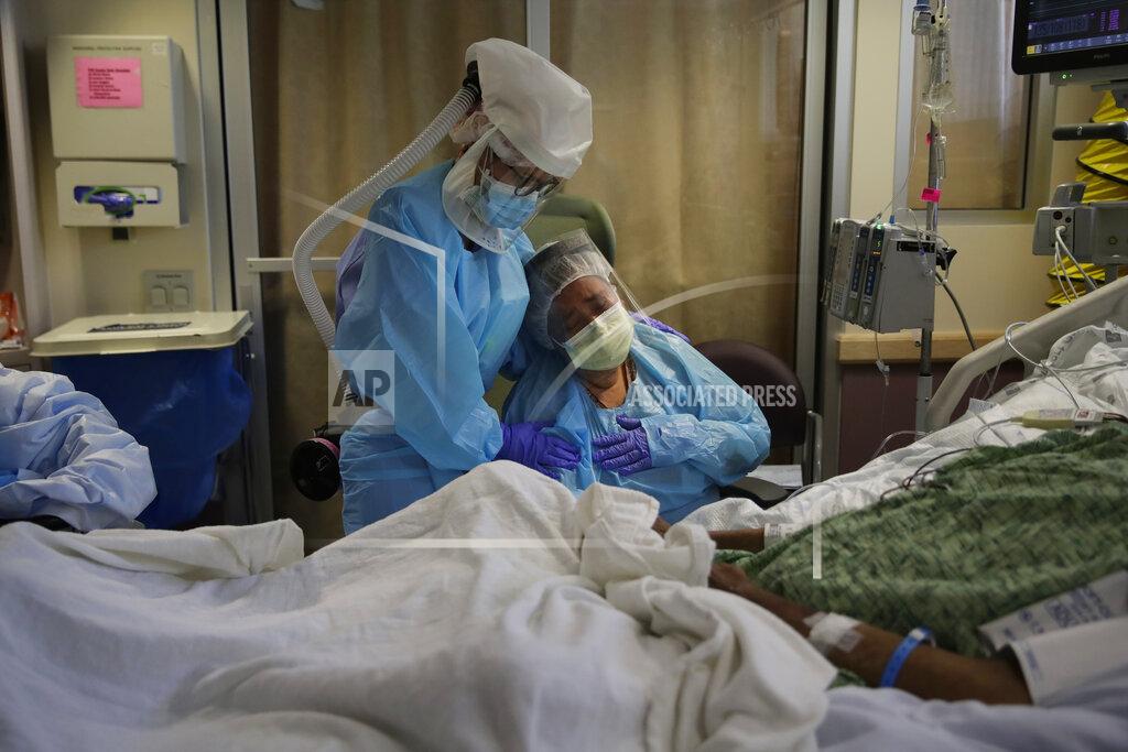 Romelia Navarro, right, is comforted by nurse Michele Younkin, left, as she weeps while sitting at the bedside of her dying husband, Antonio Navarro, in St. Jude Medical Center's COVID-19 unit in Fullerton, Calif., July 31, 2020. (AP Photo/Jae C. Hong)