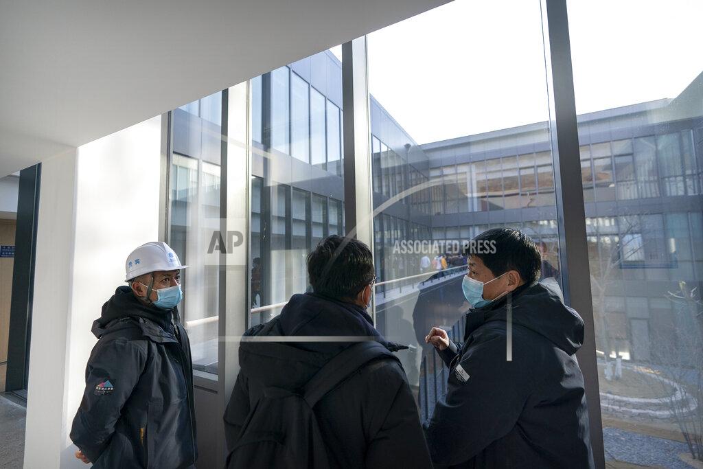 Mark Schiefelbein Workers wearing face masks to protect against the spread of the coronavirus talk in the hallway of a building at an athletes' village in Yanqing on the outskirts of Beijing, Friday, Feb. 5, 2021. Beijing Olympic organizers showed off the downhill skiing venue and the world's longest bobsled and luge track Friday, one year ahead of the scheduled opening of the 2022 Olympic Winter Games. (AP Photo/Mark Schiefelbein)