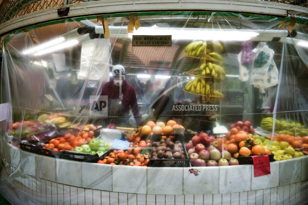 FILE - In this April 2, 2020, file photo, a worker wearing a face mask stands inside of a stall covered with a piece of plastic to prevent the spread of coronavirus, at a market in Pamplona, northern Spain. Grocery workers across the globe are working the front lines during lockdowns meant to keep the coronavirus from spreading. (AP Photo/Alvaro Barrientos, File)