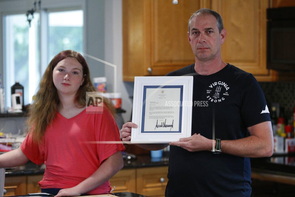 Steve Helber In this May 22, 2020, photo, Jason Nixon, right, holds a letter from President Donald Trump as he poses with his daughter, Morgan, left, as they display memorabilia from last year's shooting that took the life of Kate Nixon at their home in Virginia Beach, Va. As the shooting's one-year anniversary approaches this weekend, some of the victim's family members say the rampage is effectively forgotten. (AP Photo/Steve Helber)