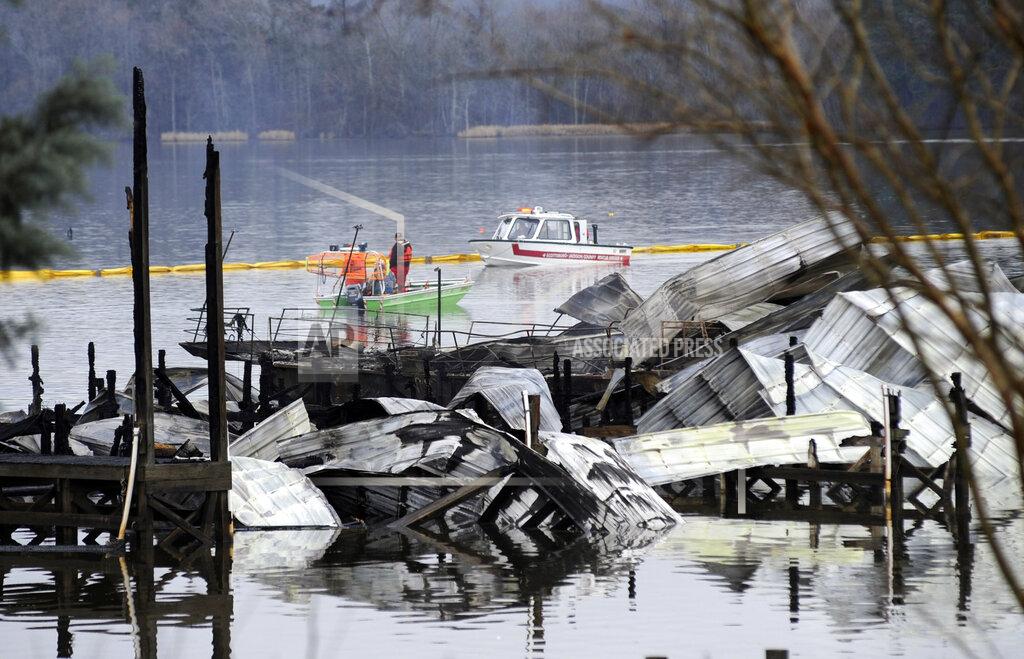 Jay Reeves FILE - In this Jan. 27, 2020 file photo, people on boats patrol near the charred remains of a dock following a fatal fire at a Tennessee River marina in Scottsboro, Ala. Authorities said the explosive fire was reported overnight while people were sleeping on boats tied up at the structure. (AP Photo/Jay Reeves, File)