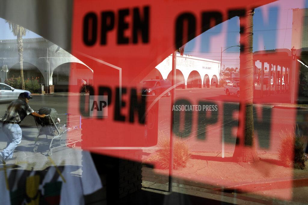 Gregory Bull FILE - In this June 30, 2020, photo, a man passes a clothing shop with open signs in the window in Calexico, Calif. A year after the first coronavirus shutdowns, many U.S. states and cities are still struggling with a silent side effect: Public records have become harder to get. As states prepared to reopen their economies following coronavirus shutdowns last spring, The Associated Press asked governors across the U.S. for records that could shed light on how businesses and health officials influenced their decisions. (AP Photo/Gregory Bull, File)