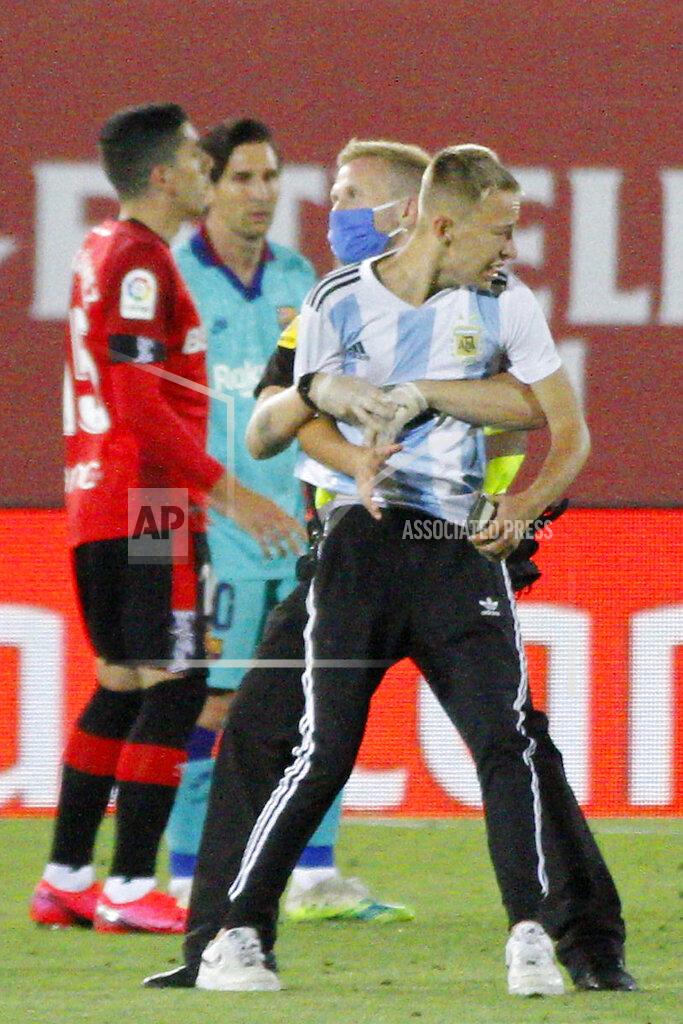 Francisco Ubilla A supporter invades the pitch with FC Barcelona's Lionel Messi behind left during the Spanish La Liga soccer match between Mallorca and FC Barcelona at Son Moix Stadium in Palma de Mallorca, Spain, Saturday, June 13, 2020. With virtual crowds, daily matches and lots of testing for the coronavirus, soccer is coming back to Spain. The Spanish league resumes this week more than three months after it was suspended because of the COVID-19 pandemic. (AP Photo/Francisco Ubilla)