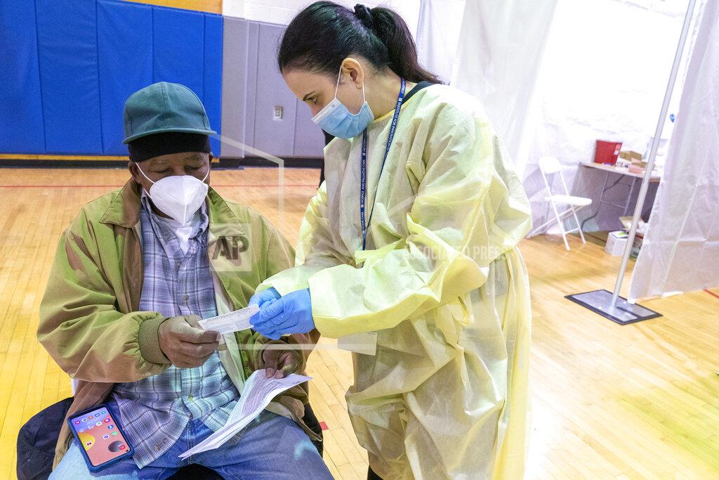 Mary Altaffer Registered Nurse Rita Alba points out to Beltran Orlando the return date on his vaccination card while he rests in the recovery area after his receiving the first dose of coronavirus vaccine at a pop-up COVID-19 vaccination site at the Bronx River Addition NYCHA complex, Sunday, Jan. 31, 2021, in the Bronx borough of New York. From elderly Cuban Americans in Florida to farmworkers in California, Latinos face daunting barriers like fear, language and a lack of education and access as the COVID-19 vaccines roll out, creating risks for public health as the virus mutates and spreads. (AP Photo/Mary Altaffer)
