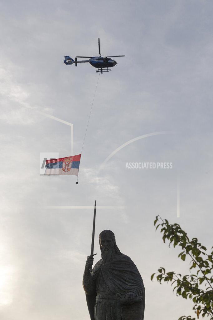 Marko Drobnjakovic A helicopter carries the flag of Serbia as it passes the collosal monument to Stefan Nemanja, a Serbian medieval ruler, during a ceremony to mark the newly established "Day of Serb Unity, Freedom and the National Flag" state holiday in Belgrade, Serbia, Wednesday, Sept. 13, 2021. Serbia has kicked off a new holiday celebrating national unity with a display of military power, triggering unease among its neighbors. (AP Photo/Marko Drobnjakovic)