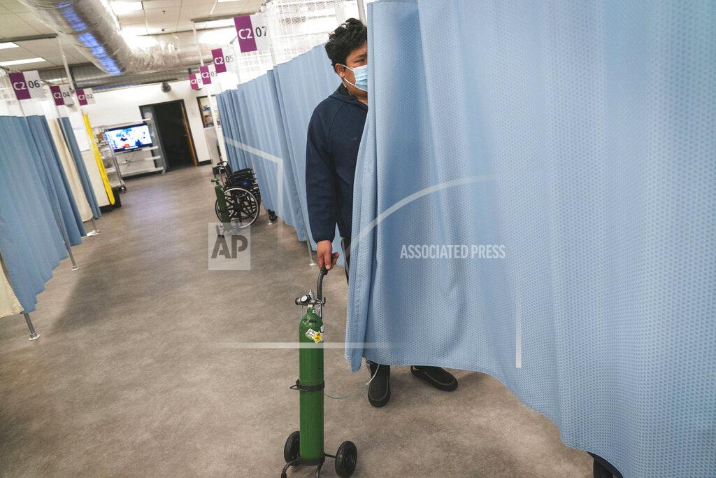 David Goldman COVID-19 patient Sall Un, 40, wheels his oxygen tank out of his room which he will take home with him as he is discharged from a field hospital set up to handle a surge of COVID-19 patients Thursday, Jan. 14, 2021, in Cranston, R.I. Un arrived at Kent Hospital's emergency room where he spent three days there in isolation heavily dependent on oxygen, before recovering enough to head to the field hospital. Eight days later he was finally discharged, walking out the backdoor to his waiting nine-year-old son, albeit with an oxygen tank in tow but on the lowest setting. (AP Photo/David Goldman)