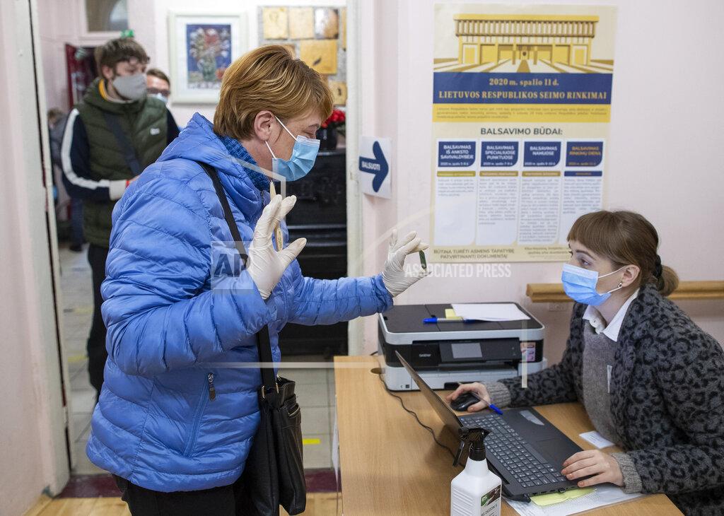 Mindaugas Kulbis A woman, wearing face masks to protect against coronavirus shows an ID card as she arrives at a polling station during parliamentary elections in Vilnius, Lithuania, Sunday, Oct.11, 2020. Polls opened Sunday for the first round of national election in Lithuania, where voters will renew the 141-seat parliament and the ruling four-party coalition is widely expected to face a stiff challenge from the opposition to remain in office. (AP Photo/Mindaugas Kulbis)