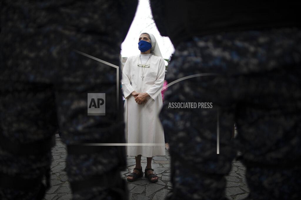 Ariana Cubillos A nun stands behind police creating a perimeter for a Holy Week procession by devotees of the "Nazareno de San Pablo" statue of Jesus before it passes through in a popemobile amid the COVID-19 pandemic in Caracas, Venezuela, Wednesday, March 31, 2021. The annual procession wasn't allowed for the second year in a row to help contain the spread of the new coronavirus. (AP Photo/Ariana Cubillos)