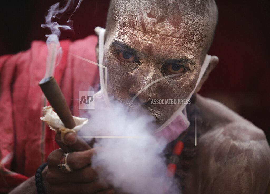 Karma Sonam A Naga Sadhu or Naked Hindu holy man smokes before taking a holy dips in the river Ganges during Shahi snan or a Royal bath during Kumbh mela, in Haridwar in the Indian state of Uttarakhand, Monday, April 12, 2021. As states across India are declaring some version of a lockdown to battle rising Covid cases as part of a nationwide second-wave, thousands of pilgrims are gathering on the banks of the river Ganga for the Hindu festival Kumbh Mela. The faithful believe that a dip in the waters of the Ganga will absolve them of their sins and deliver them from the cycle of birth and death. (AP Photo/Karma Sonam)