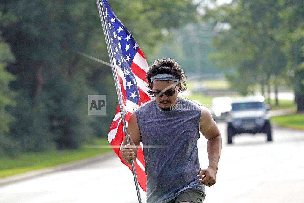 A man, who identifies himself as Dom, jogs along a road with an American flag Saturday, July 4, 2020, in Houston. (AP Photo/David J. Phillip)