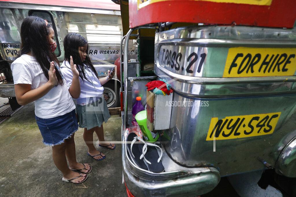 Aaron Favila Grade school students Bhea Joy Roxas, right, and Elrich Joy, left, use a smart phone as they raise their hands while reciting the "Panatang Makabayan" or Patriotic Oath during the opening of classes at the Tandang Sora jeepney terminal in Quezon city, Philippines on Monday, Oct. 5, 2020. Students in the Philippines began classes at home Monday after the coronavirus pandemic forced remote-learning onto an educational system already struggling to fun schools. The two students missed the flag raising ceremony due to poor internet connection. (AP Photo/Aaron Favila)