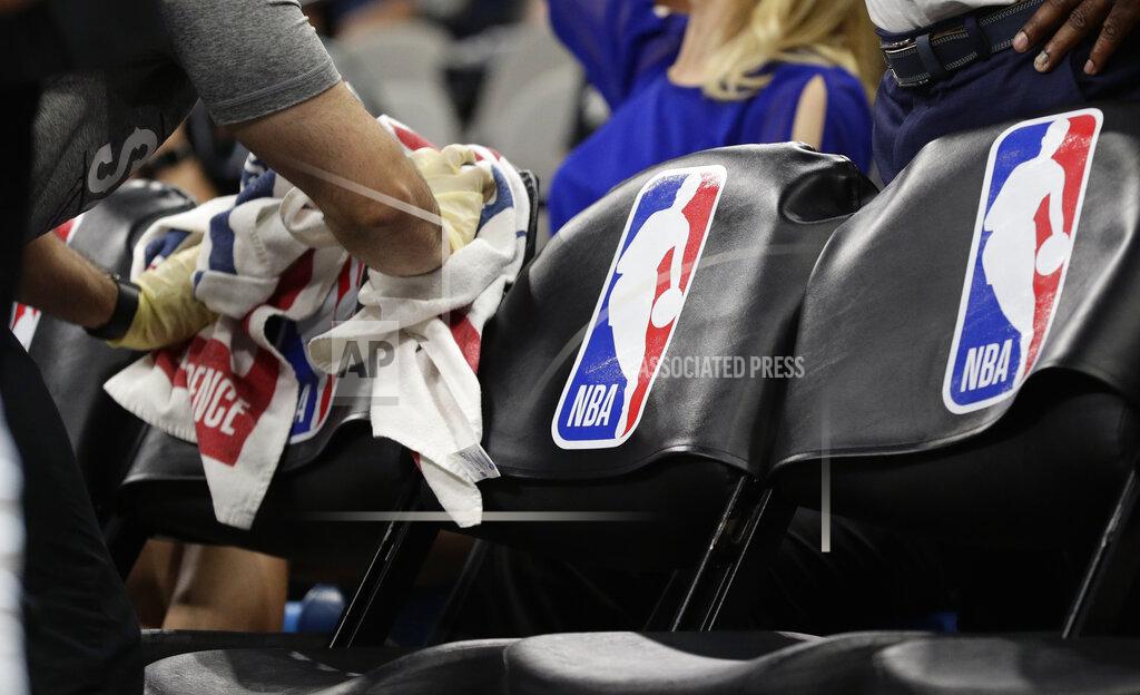 A team attendant uses protective gloves to wipe down seats in the players' bench area during an NBA basketball game between the San Antonio Spurs and the Dallas Mavericks in San Antonio, Tuesday, March 10, 2020. (AP Photo/Eric Gay)