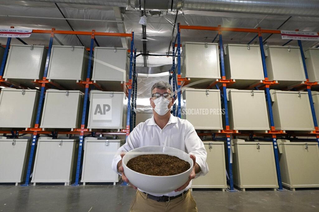 Ted S. Warren Micah Truman, CEO of Return Home, a company that composts human remains into soil, poses for a photo, Wednesday, Sept. 15, 2021, in Auburn, Wash., south of Seattle. Truman is holding a container of soil made with animal remains that is used to show what the product of their process looks like. Behind him are the metal vessels where bodies are kept during the first month of the two-month composing process. Earlier in September, Colorado became the second state after Washington to allow human body composting, and Oregon will allow the practice beginning next July. (AP Photo/Ted S. Warren)
