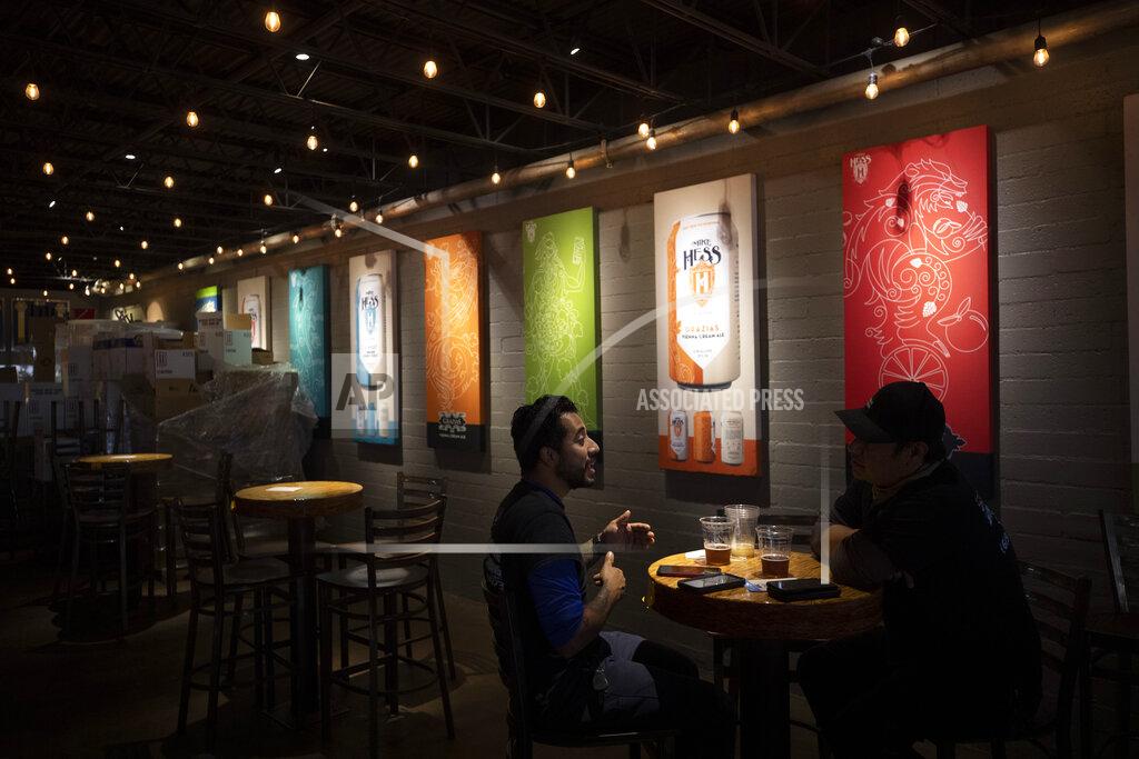 FILE - In this June 29, 2020, file photo, two men drink beers at the Mike Hess brewery and tasting room in San Diego. Authorities are closing honky tonks, bars and other drinking establishments in some parts of the U.S. to stem the surge of COVID-19 infections — a move backed by sound science about risk factors that go beyond wearing or not wearing masks. (AP Photo/Gregory Bull, File)