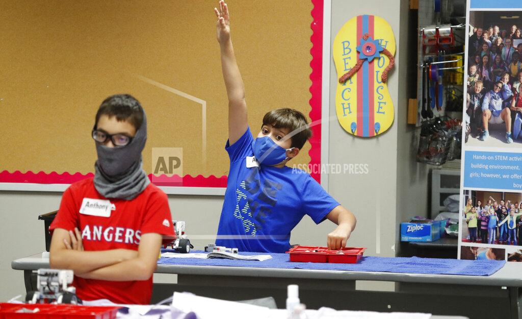FILE - In this Tuesday, July 14, 2020 file photo, Amid concerns of the spread of COVID-19, Aiden Trabucco, right, wears a mask as he raises his hand to answer a question behind Anthony Gonzales during a summer STEM camp at Wylie High School in Wylie, Texas.Most of the 85 young children in a South Texas county who are known to have contracted the coronavirus tested positive this month amid a surge in the state, a health official said Sunday, July 19, 2020. (AP Photo/LM Otero, File)