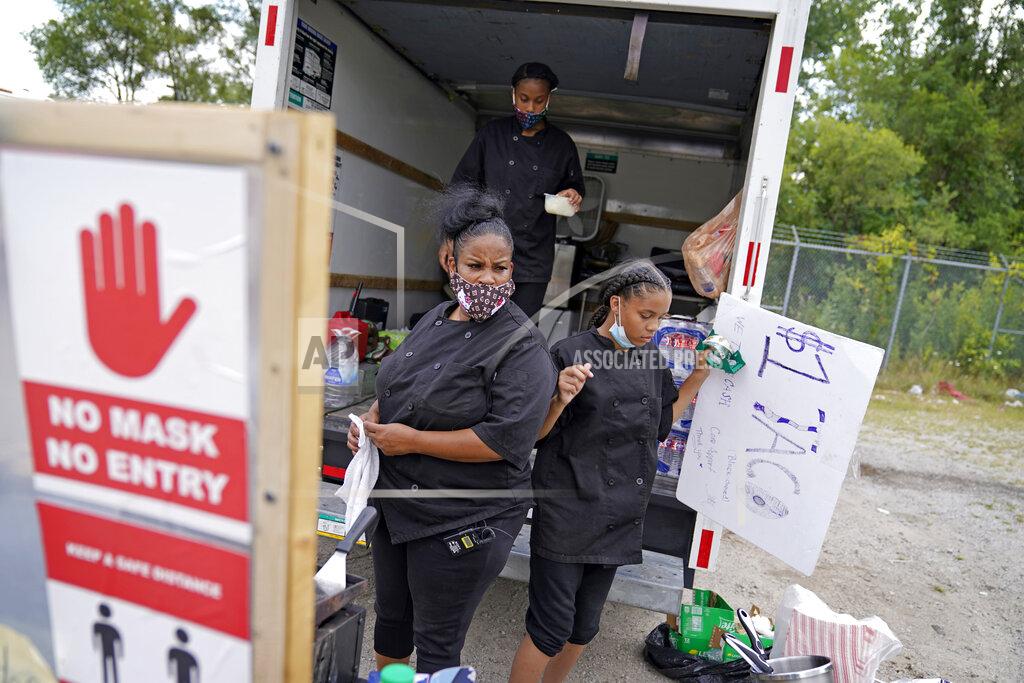 David Goldman Tequila Butler, left, sets up her taco stand out of the back of a U-Haul truck with her daughters, Alliyah, 15, rear, and Chardonnay, 14, in the Auburn Gresham neighborhood in Chicago, Thursday, Aug. 27, 2020. Butler suspects she was infected with the virus this spring after she was transferred from her job in a hospital kitchen to one cleaning COVID-19 patients' rooms. After she was furloughed, she decided not to go back. So the culinary school graduate converted a rented U-Haul into a truck that sells $1 tacos, the low price to accommodate customers with little money.(AP Photo/David Goldman)