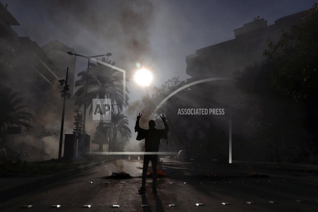 Bilal Hussein FILE - In this Feb. 24, 2021 file photo, a protester flashes the victory sign, as others burn tires to block a road in front of the house of judge Fadi Akiki during a demonstration calling for the release of anti-government activists detained following riots in northern Lebanon late last month, in Beirut, Lebanon. A public feud in recent weeks among prosecutors has starkly demonstrated how Lebanon's system of sectarian factions is paralyzing Lebanon's judicial system and snarling attempts to root out corruption. (AP Photo/Bilal Hussein, File)