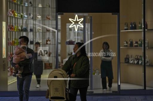 FILE - A couple with their toddler walk by as sales promoters wait for customers at a fashion bag boutique at an outdoor shopping mall in Beijing, on Nov. 12, 2023. China's economy showed more signs of reviving in October as retail sales and manufacturing picked up though the property sector remained sluggish, the government said Wednesday, Nov. 15. (AP Photo/Andy Wong, File)